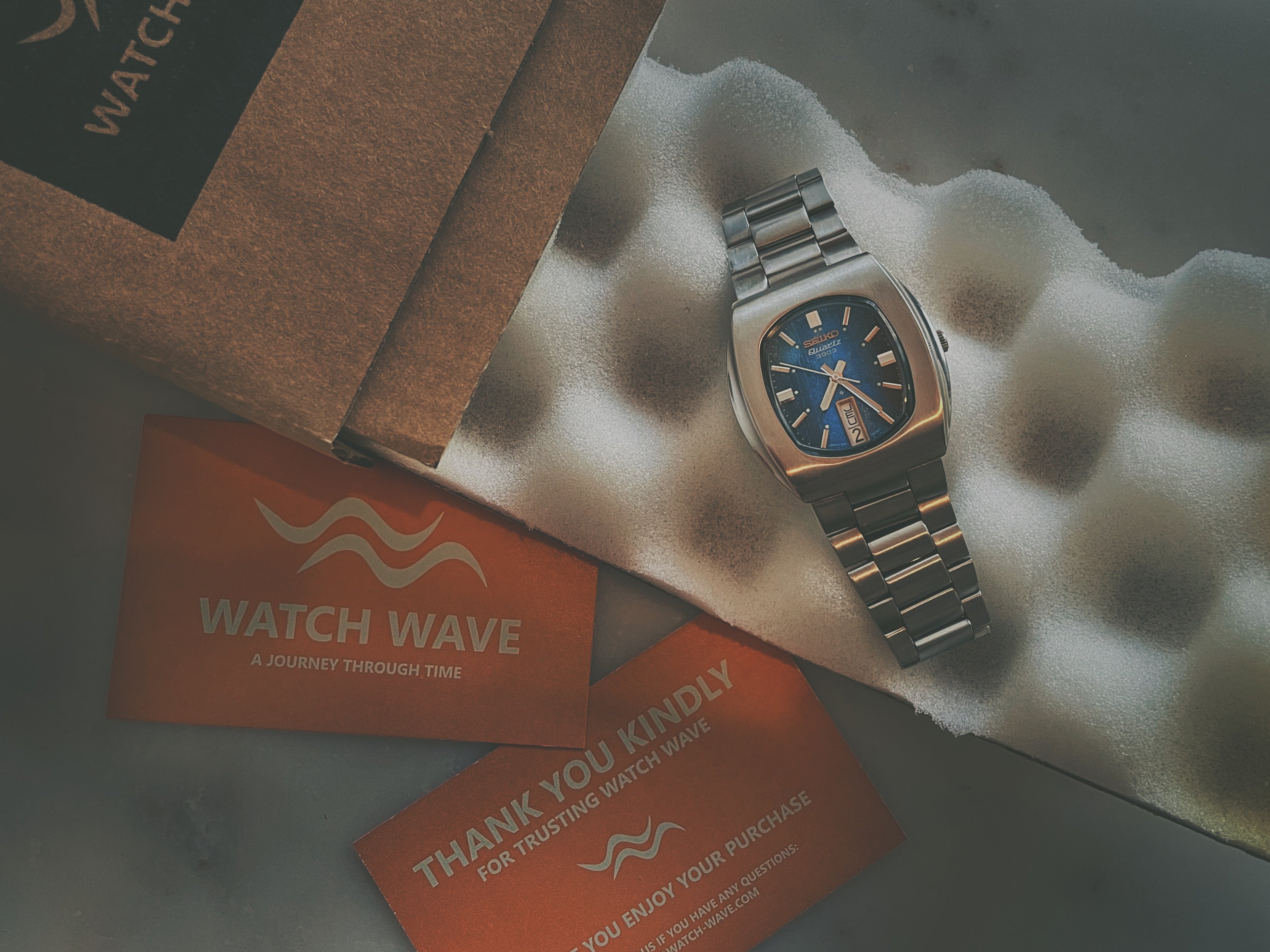 A vintage Seiko laying on a shipping box with a WATCH WAVE business card next to it